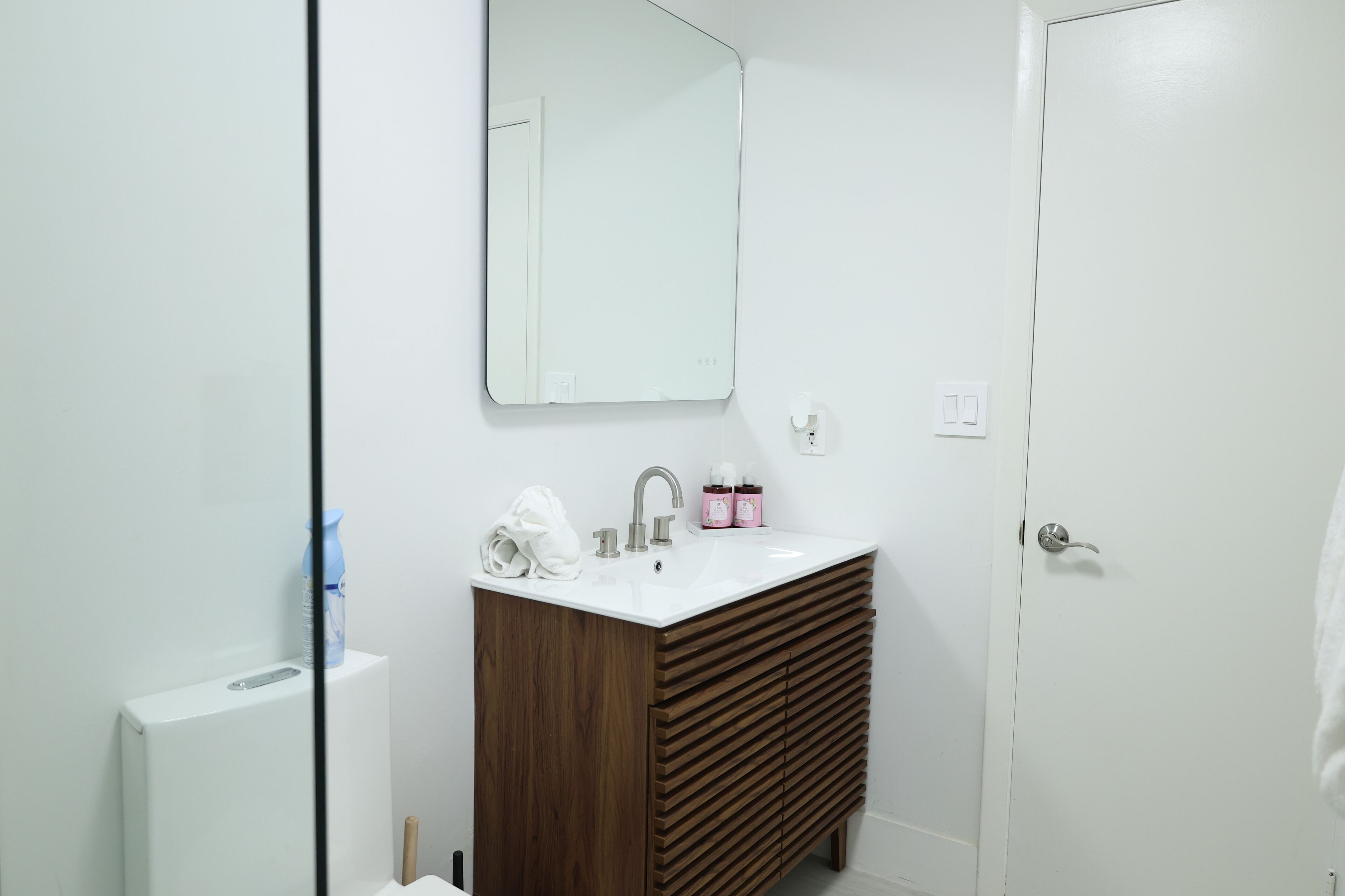 A bathroom with a white sink, wooden vanity, and a mirror.