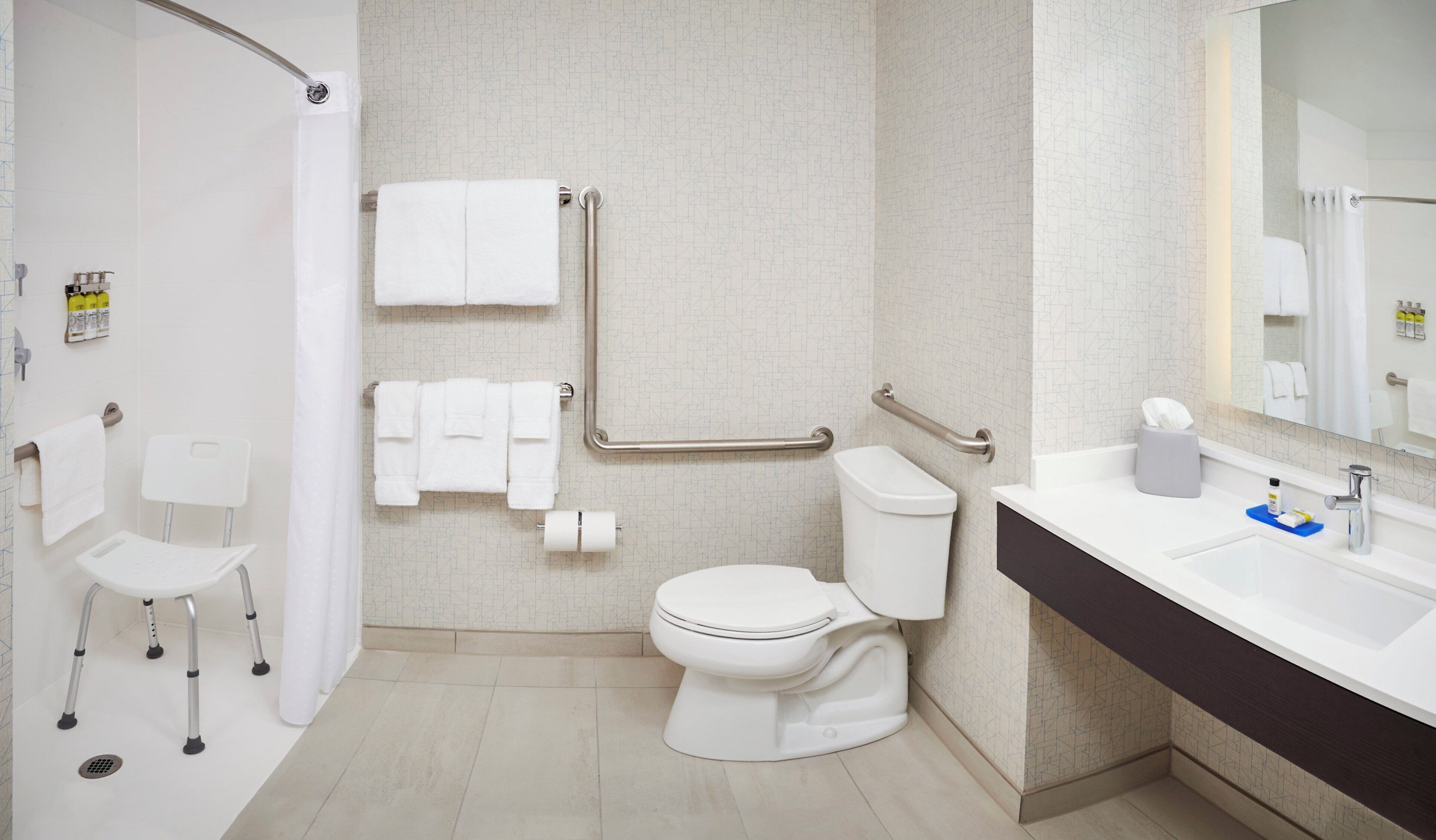 Een moderne badkamer met toilet, bidet, handgrepen, een stoel en een wastafel met toiletartikelen.