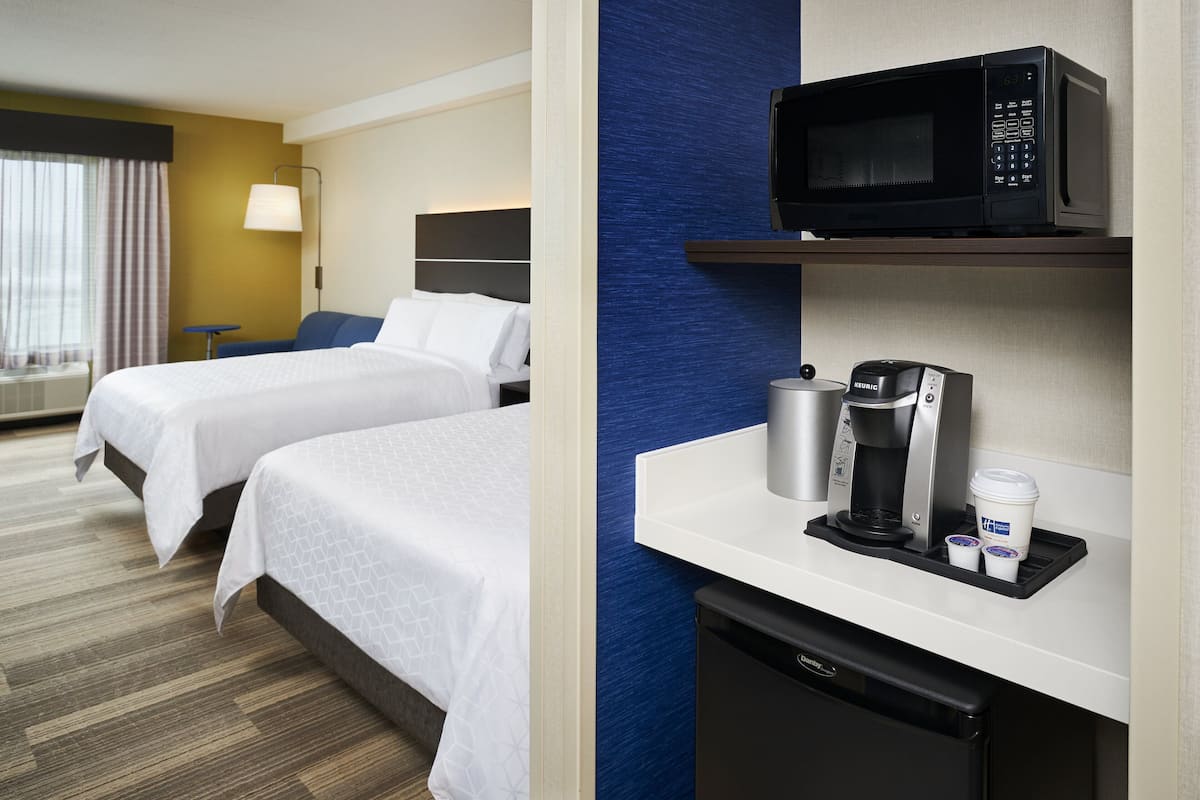 A hotel room with two beds, a microwave, a coffee maker, and a mini fridge.