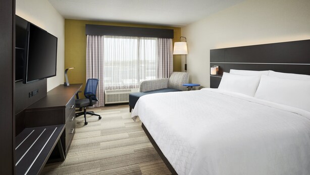 A hotel room with a large bed, a desk with a flat-screen TV, a chair, a small table, and a window with curtains. - Holiday Inn Express & Suites Windsor East - Lakeshore by IHG (Lakeshore)