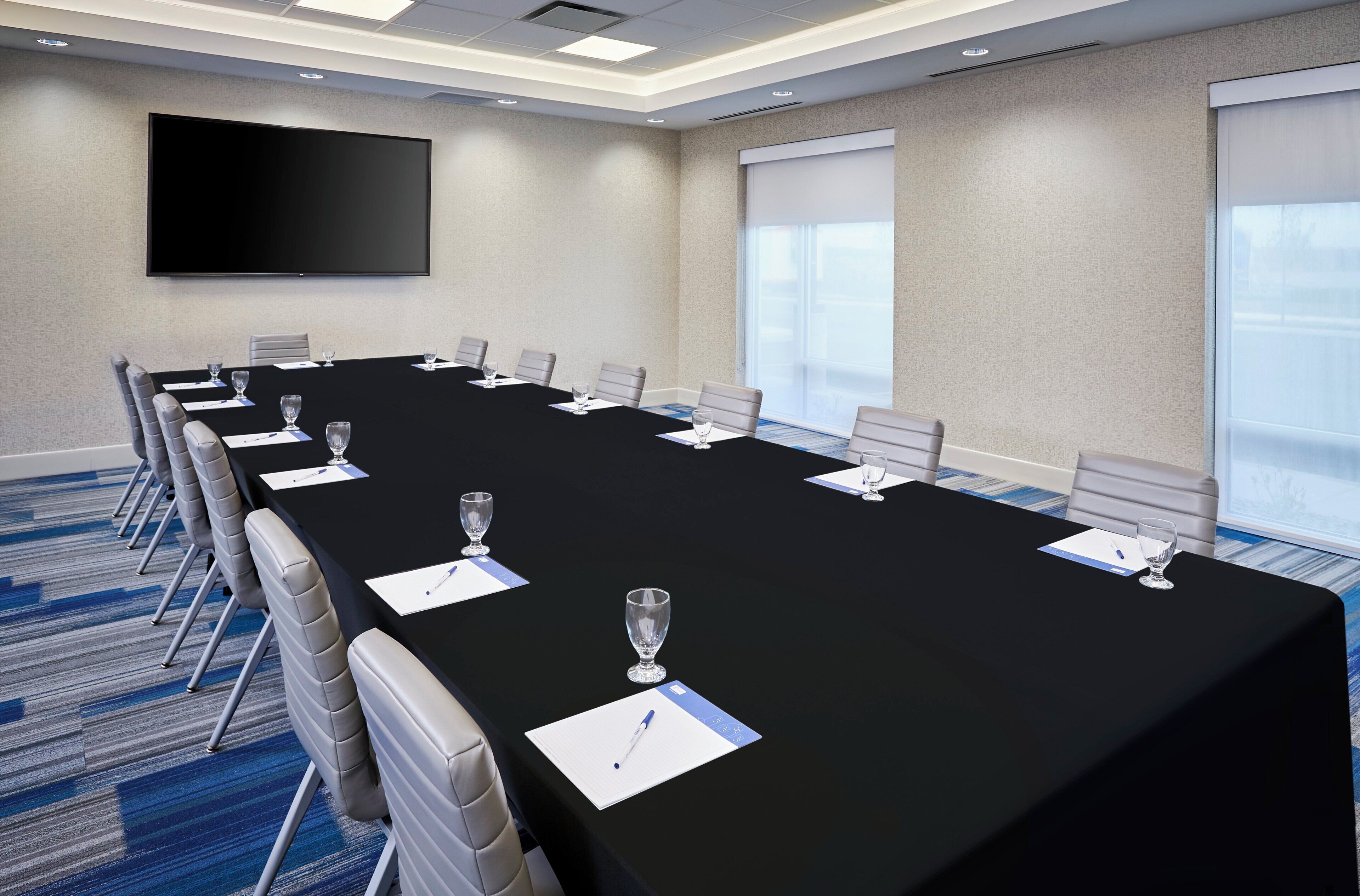 A conference room with a long table, chairs, a flat-screen TV, and large windows.