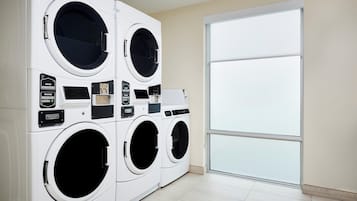 A laundry room with four white front-loading washing machines and a large sliding glass door.