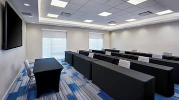 Un salón de conferencias con una mesa larga, varias sillas, un televisor de pantalla plana y piso alfombrado.