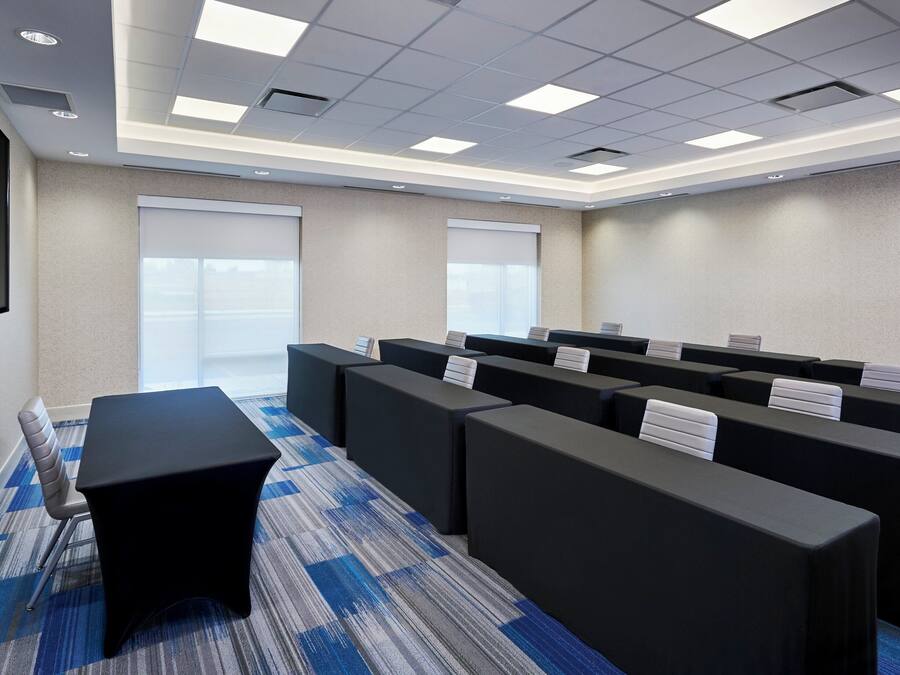 Un salón de conferencias con una mesa larga, varias sillas, un televisor de pantalla plana y piso alfombrado.