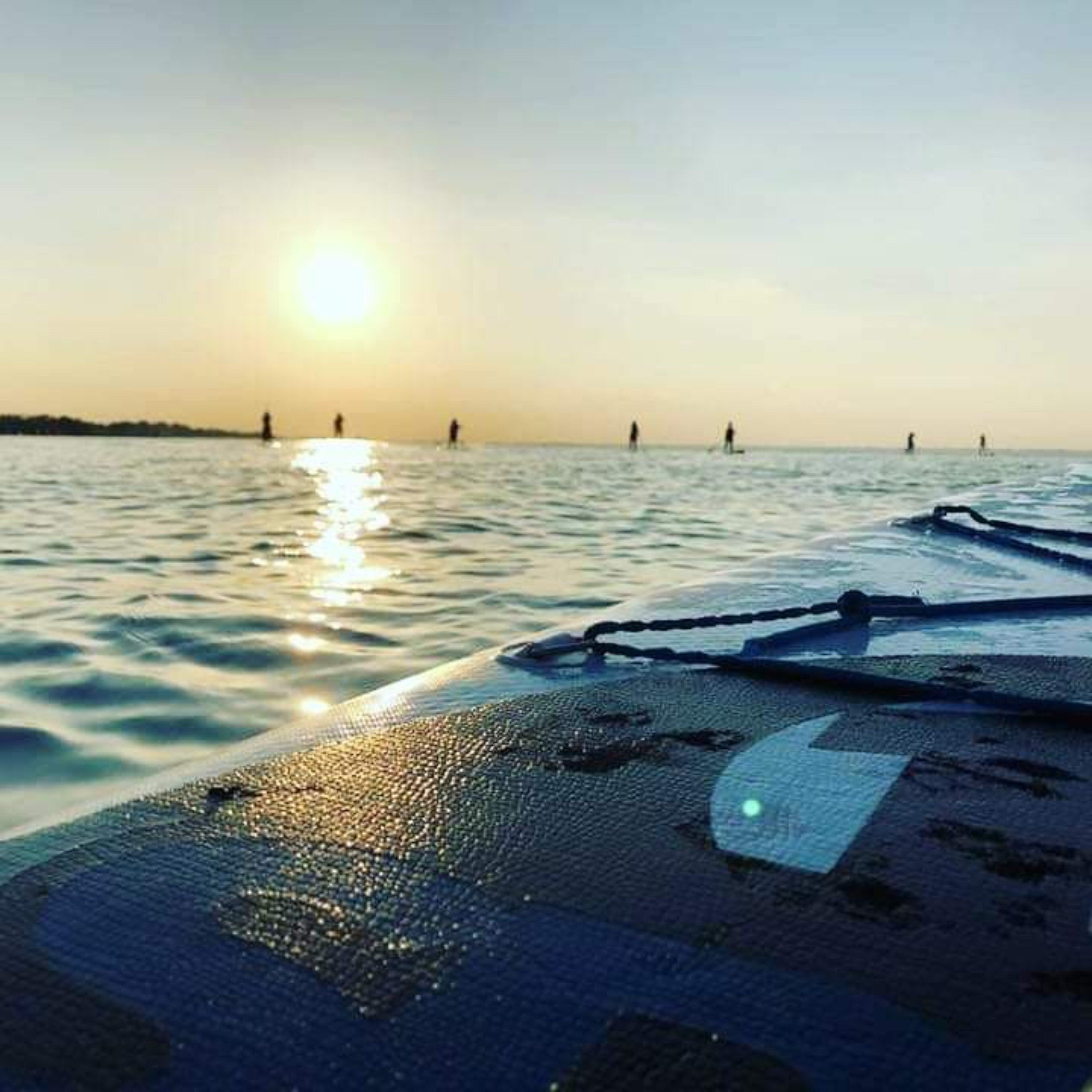 Cubierta de barco con vista al agua y el sol poniéndose en la distancia.