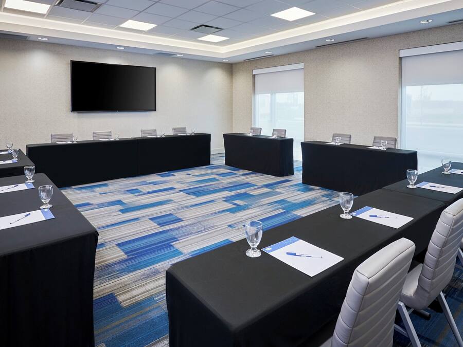 A conference room with a large flat-screen TV, multiple tables with chairs, and a carpeted floor.