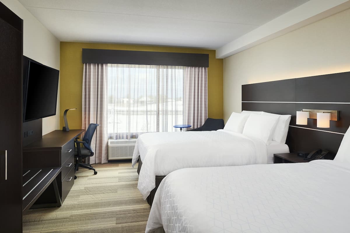 A hotel room with two beds, a desk with a chair, a TV, and a window with curtains.
