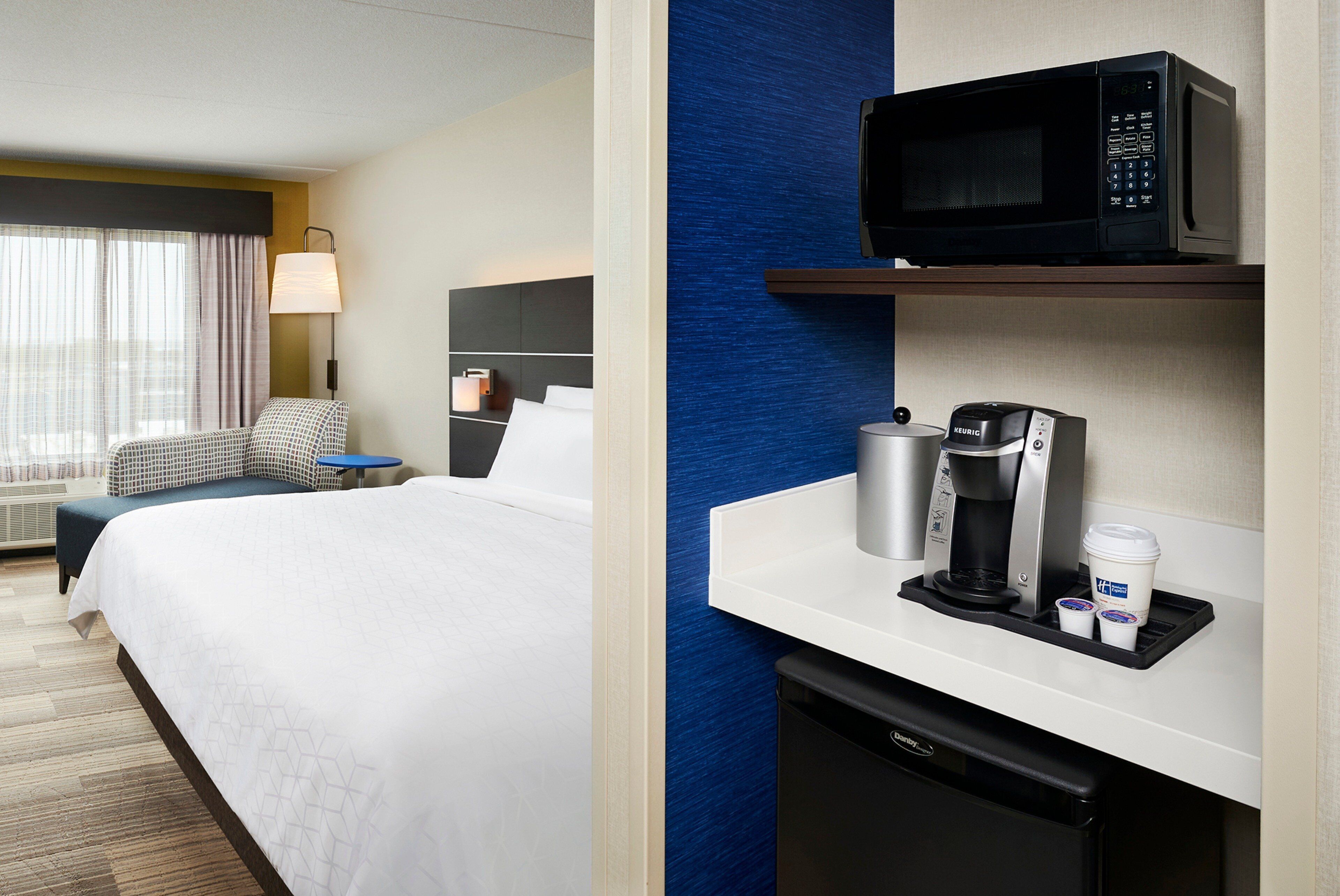 Habitación de hotel con cama, escritorio con cafetera, microondas y refrigerador pequeño.