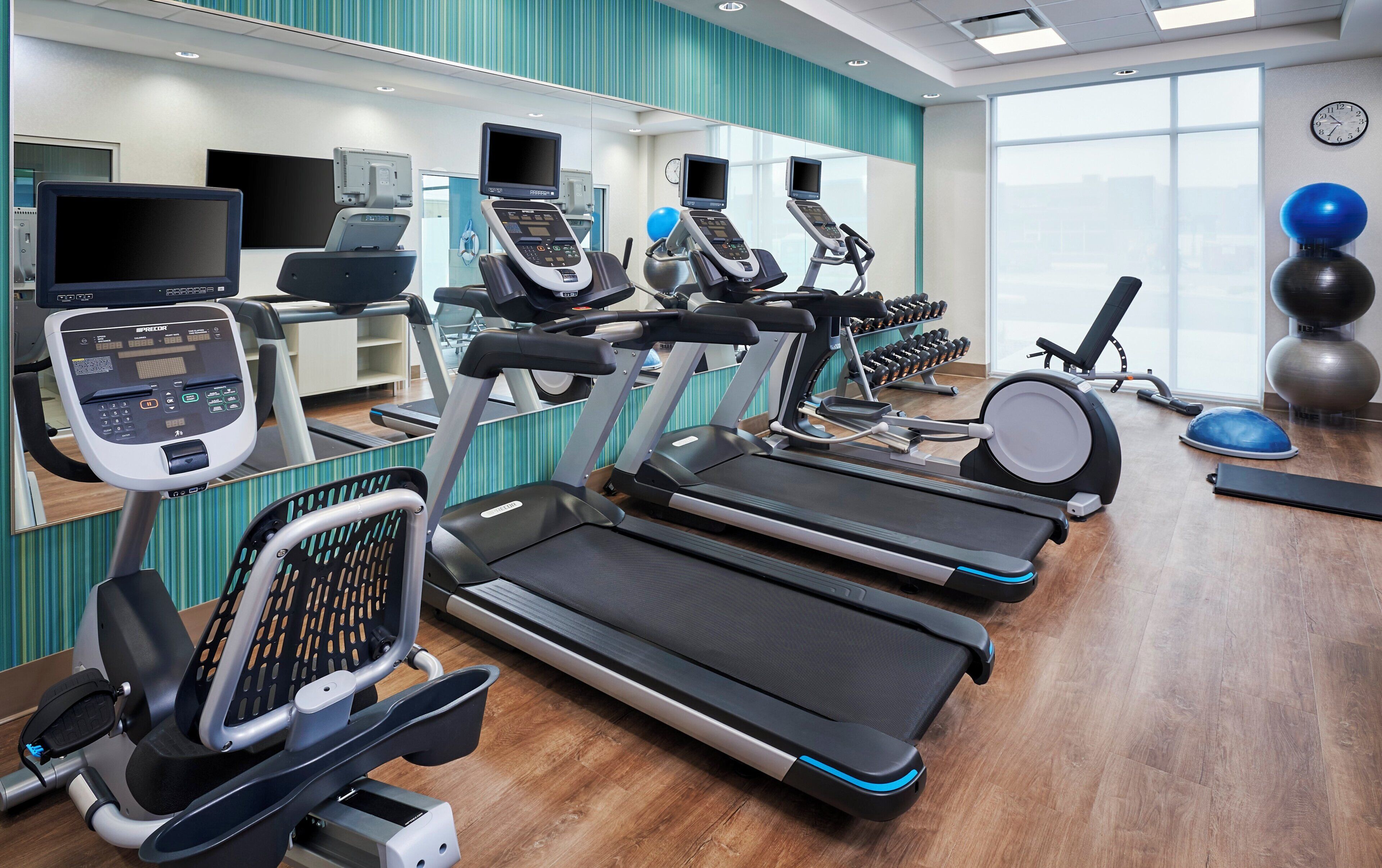 Une salle de sport équipée de tapis de course, de vélos elliptiques et de ballons d’exercice.