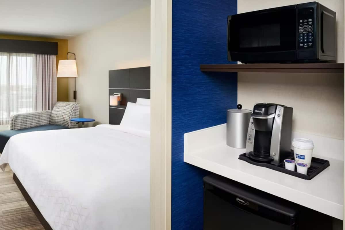 A hotel room with a bed, a desk, a microwave, a coffee maker, and a trash bin.