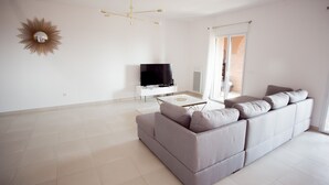 A modern living room with a grey sofa, a flat-screen TV, a white coffee table, and a sunburst mirror on the wall. - A breathtaking view 5 minutes from the Chateau de Brégancon (La Londe-les-Maures)