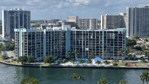 A waterfront hotel with multiple high-rise buildings in the background, a parking lot, and palm trees along the water's edge. - 16th Floor  Beachfront Condo at the Sea Air Tower (Hollywood/Hallandale Beach)