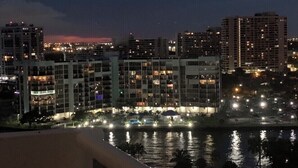 Nachtansicht einer Stadt mit beleuchteten Gebäuden und einem sich spiegelnden Gewässer.