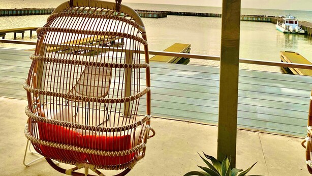 A wicker swing chair overlooking a waterfront with a boat dock.