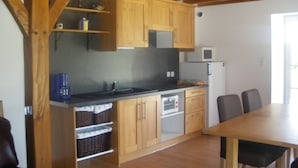 Una cocina con armarios de madera, un microondas y un lavamanos. Hay una mesa de comedor con sillas.