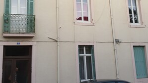 Ein mehrgeschossiges Gebäude mit mehreren Fenstern, einige mit Fensterläden, und einer sichtbaren Tür mit einer Nummer.