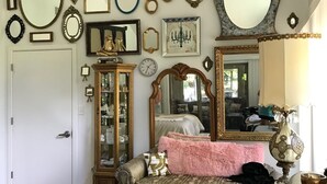 A room with a variety of mirrors and picture frames on the wall, a bed with a pink blanket, and a dresser with a lamp. - Great Location close to everything (Texarkana)