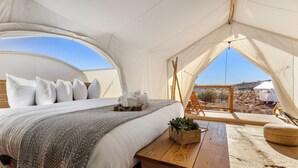 Alojamiento en tienda de campaña con cama, mesa de madera y vistas al paisaje.