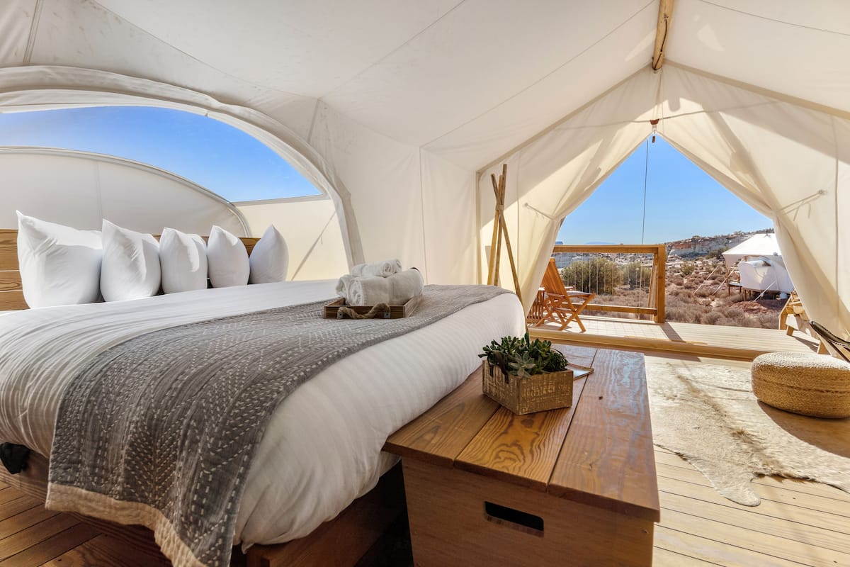 Een tentaccommodatie met een bed, houten tafel en uitzicht op het landschap.