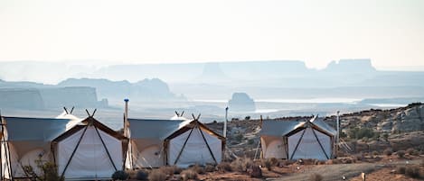 A desert landscape with multiple tents set up in a row, suggesting a campsite or temporary accommodation area.