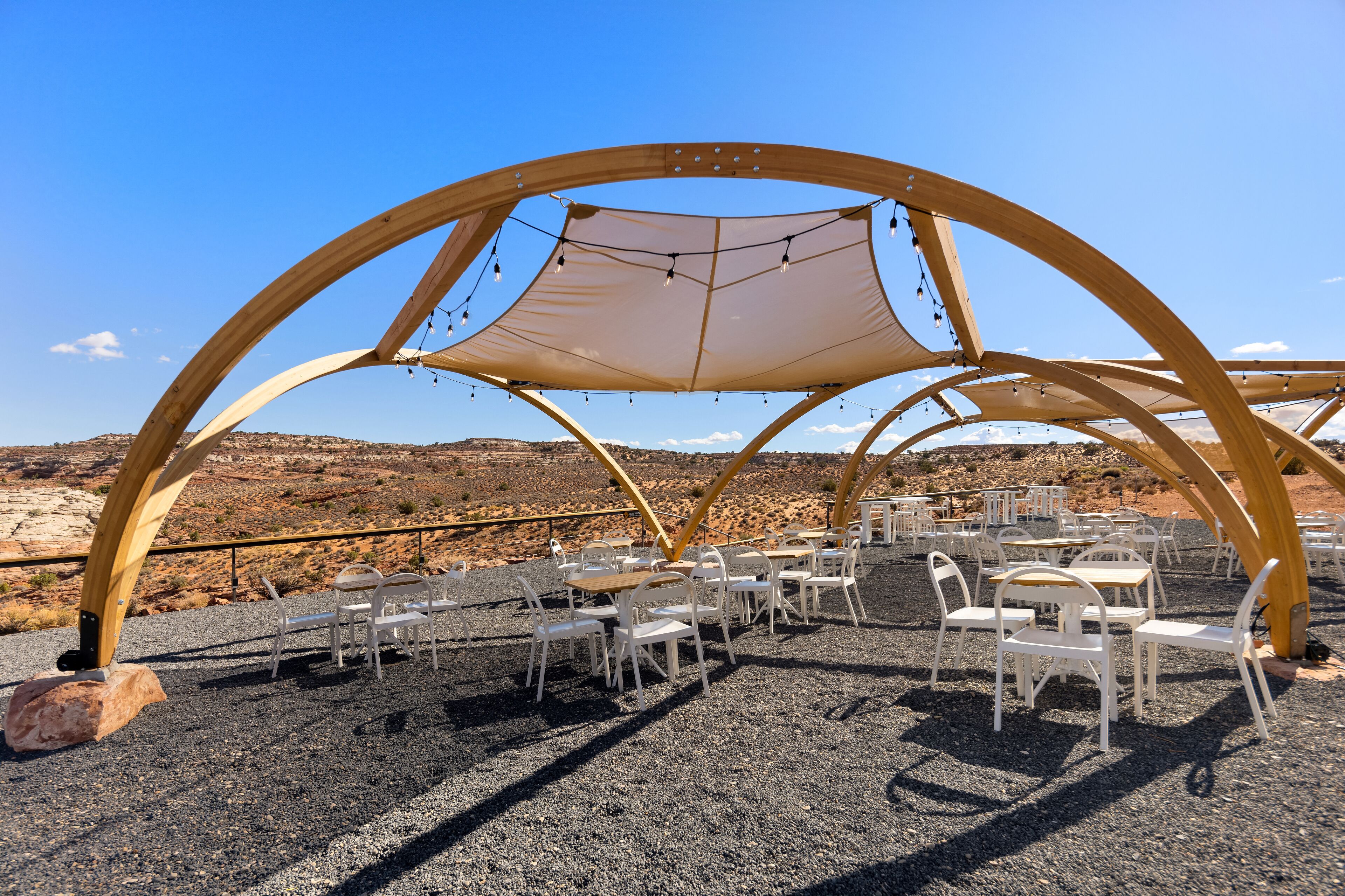 An outdoor seating area with tables and chairs under a wooden canopy structure.
