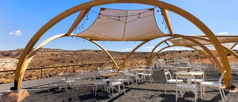 An outdoor seating area with tables and chairs under a wooden canopy structure.