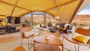 A tented accommodation with a central seating area, a clothing rack, and a view of the desert landscape.