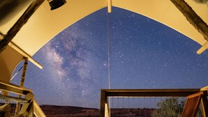 Cielo estrellado visto desde una terraza de madera con una silla y leña apilada.