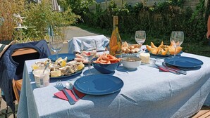 Mesa para comer al aire libre dispuesta con platos, tazones y vasos, rodeada de vegetación y una valla de madera.