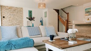 Una sala de estar acogedora con una pared de piedra, una escalera de madera y una chimenea.