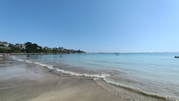 Una playa con agua cristalina, una orilla de arena y edificios al fondo.
