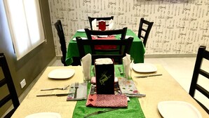 Mesa de comedor preparada para cuatro personas, con camino de mesa verde, platos blancos y sillas negras.