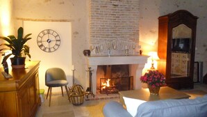 A cozy living room with a fireplace, a clock, and a sofa. - Gîte en Sancerrois (Menetou-Râtel)