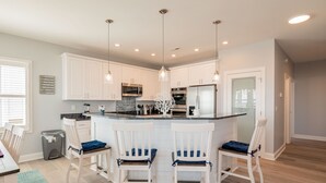 A modern kitchen with white cabinetry, a central island with bar stools, and pendant lighting. - Ocean Wind: Kid-friendly and Dog-friendly Ocean View Home with Private Pool (Oak Island)