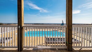 A wooden deck with a pool, white railing, and a view of the beach. - Ocean Wind: Kid-friendly and Dog-friendly Ocean View Home with Private Pool (Oak Island)