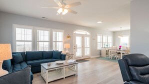A spacious living room with a dark blue sofa, a white coffee table, and a ceiling fan. - Ocean Wind: Kid-friendly and Dog-friendly Ocean View Home with Private Pool (Oak Island)