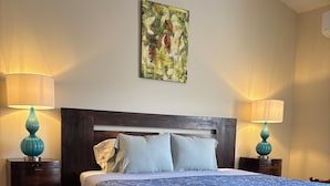 Un dormitorio con una cama de madera, dos mesitas de noche con lámparas, un cuadro en la pared y suelo de baldosas.