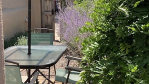 Un patio al aire libre con una mesa, sillas, una sombrilla y una puerta que da a un vehículo.