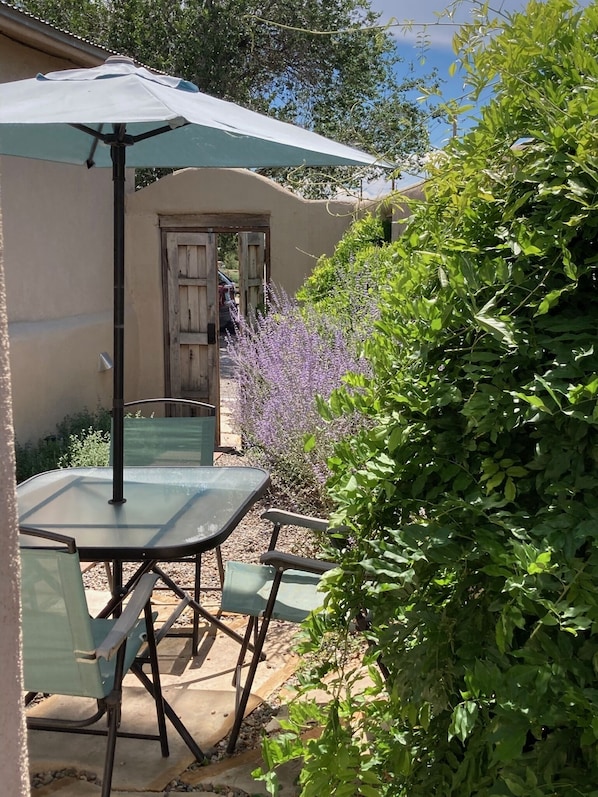 Een terras buiten met een tafel, stoelen, een overdekte parasol en een deur die naar een voertuig leidt.