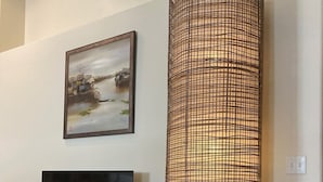 Una sala de estar con un televisor sobre un mueble de madera, una lámpara trenzada grande y un cuadro enmarcado en la pared.