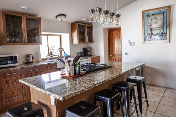 Une cuisine moderne dotée de plans de travail en granit, d’armoires en bois et d’un grand îlot central avec des tabourets de bar.
