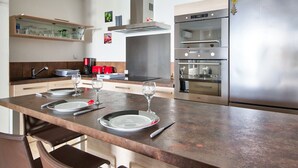 A modern kitchen with a stainless steel refrigerator, double oven, and a built-in range hood. - Appartement Gimelli – Welkeys (Toulon)
