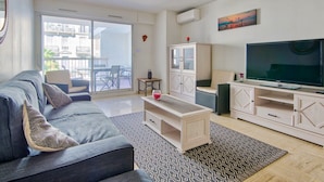 A modern living room with a grey sofa, a coffee table, a TV, and a balcony with outdoor furniture. - Appartement Gimelli – Welkeys (Toulon)