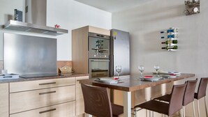 A modern kitchen with a dining area, stainless steel appliances, wooden cabinets, and a bar area with wine bottles. - Appartement Gimelli – Welkeys (Toulon)
