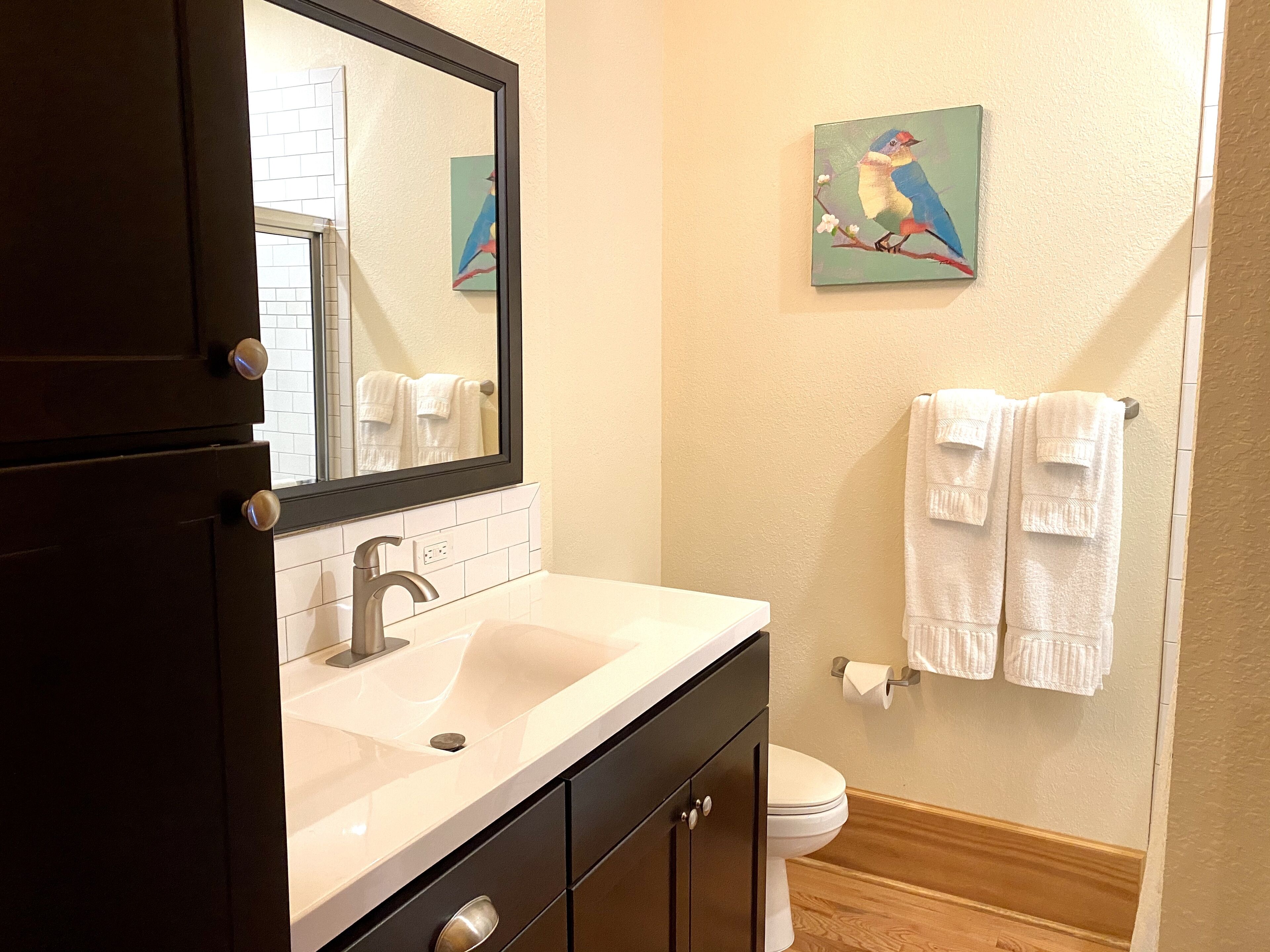 A bathroom with a white sink, dark cabinets, a mirror, a toilet, and two towels hanging on the wall.