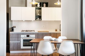A modern kitchen with white cabinetry, a built-in oven, and a dining area with a wooden table and white chairs.