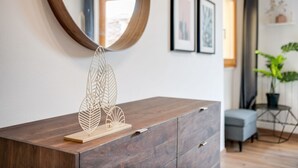 A wooden dresser with a leaf-shaped decorative piece on top, a round mirror, and framed artwork on the wall.