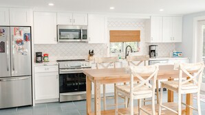 Een moderne keuken met witte kastjes, roestvrijstalen apparatuur en een houten eettafel met stoelen.