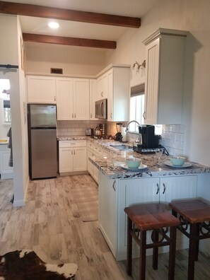 A kitchen with white cabinets, a stainless steel refrigerator, a microwave, a sink, and a wooden island with stools.