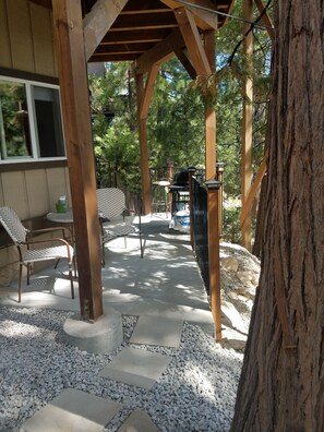 A covered patio with outdoor furniture, a grill, and a stone pathway.